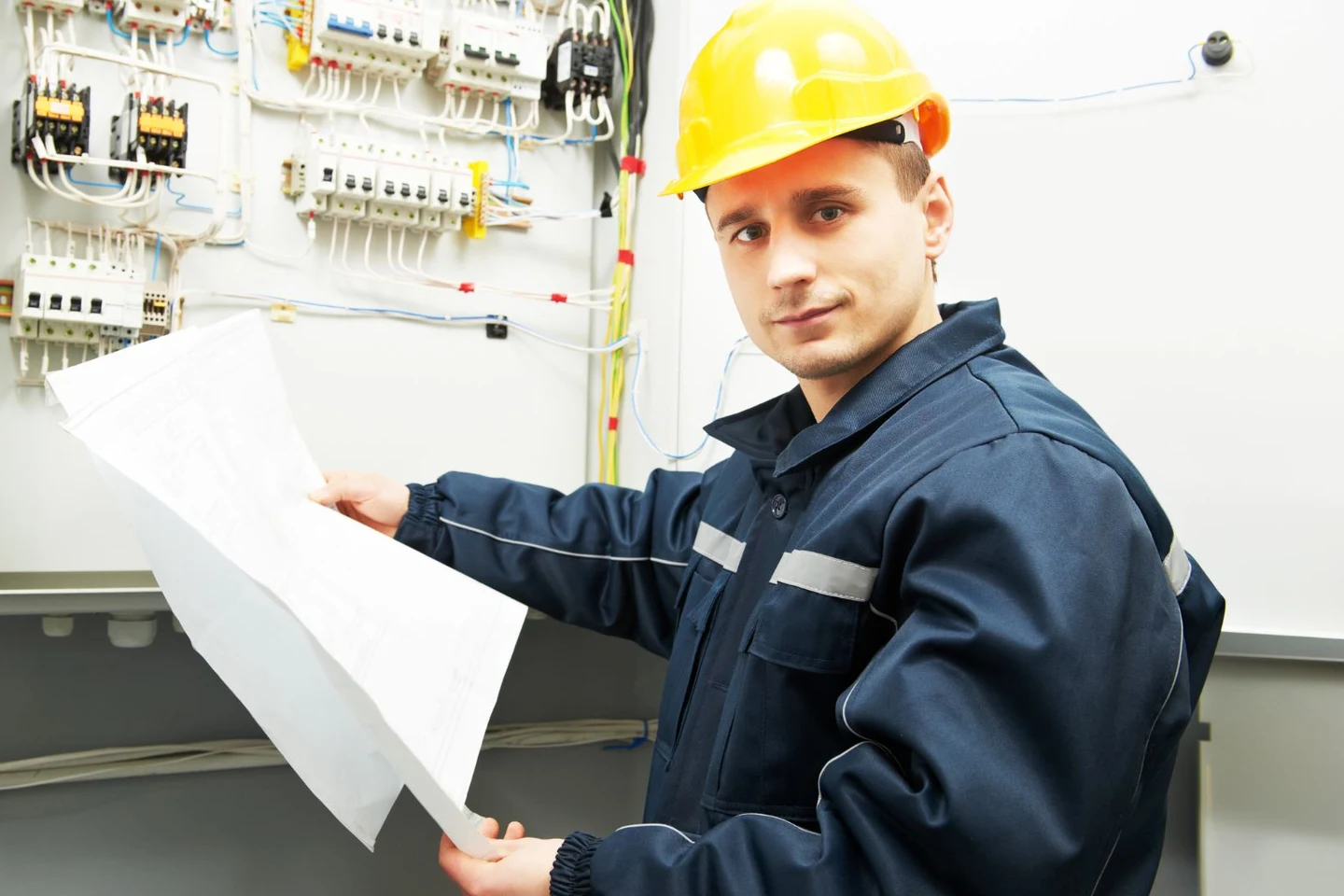 Elektrofachkraft prüft Unterlagen vor einer geöffneten Verteilung