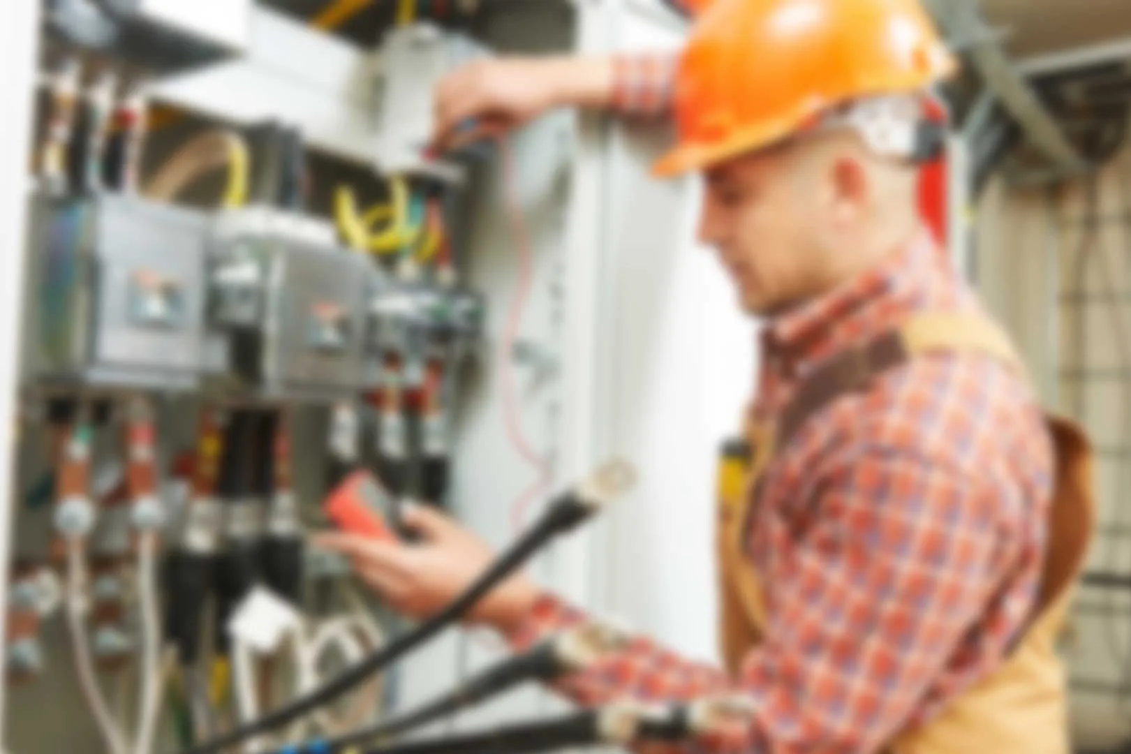 Elektrofachkraft mit Helm und Gehörschutz an einer Schaltanlage