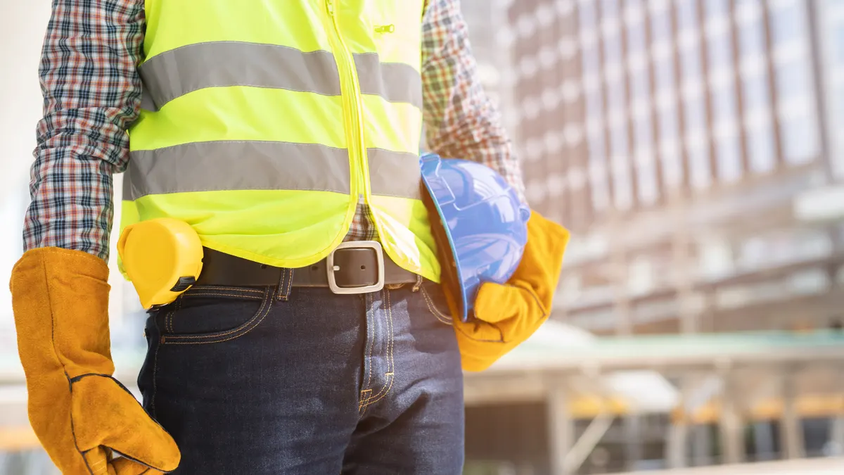 Beschäftigter mit Warnweste, Schutzhelm und Arbeitshandschuhen